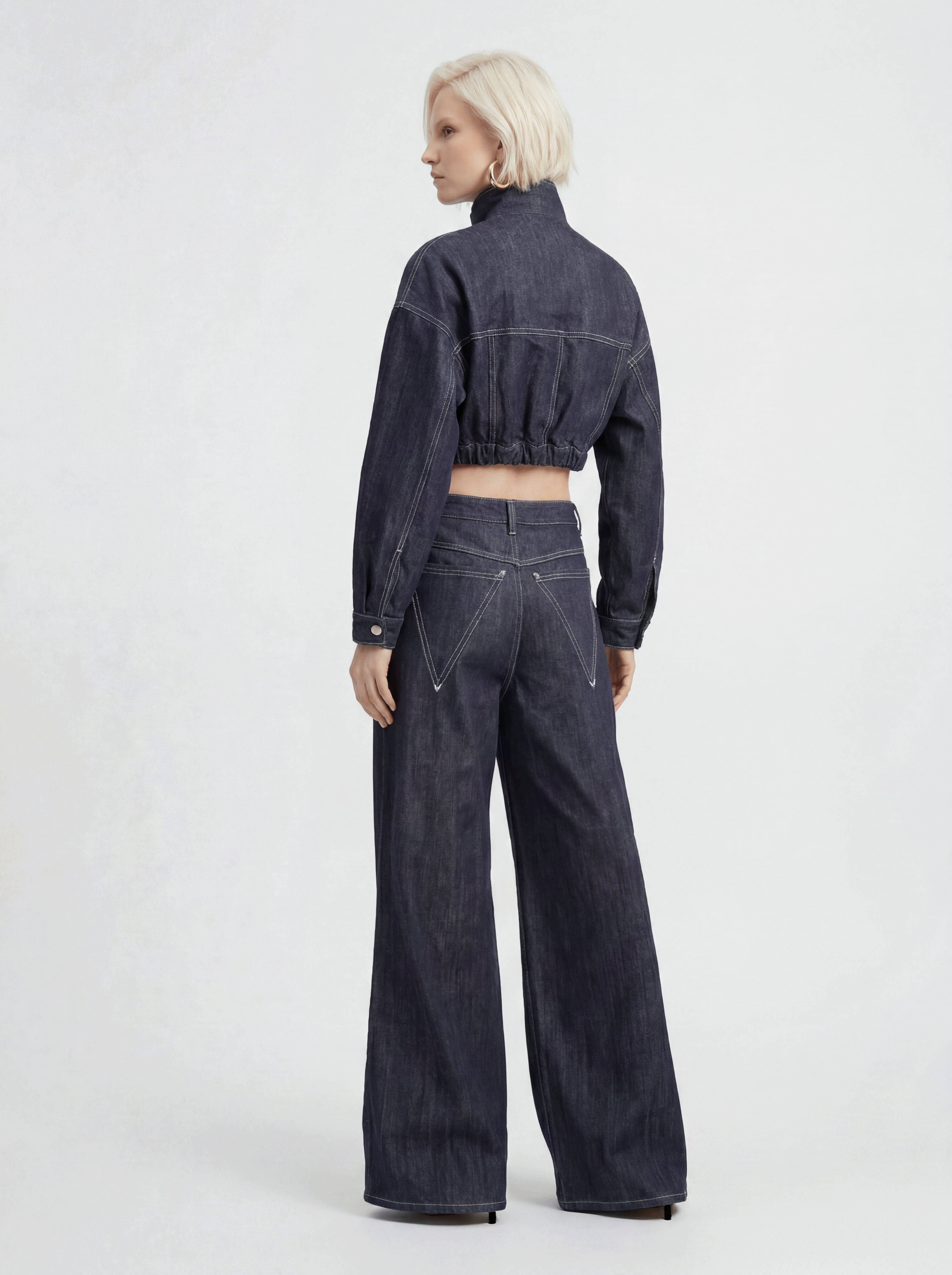 Back view of model wearing LA GIACCA CORTA IN DENIM and IL DENIM TRIANGOLO by ORNELLA COLICCHIO, looking to the side and showing the back of the denim jacket and triangular pockets