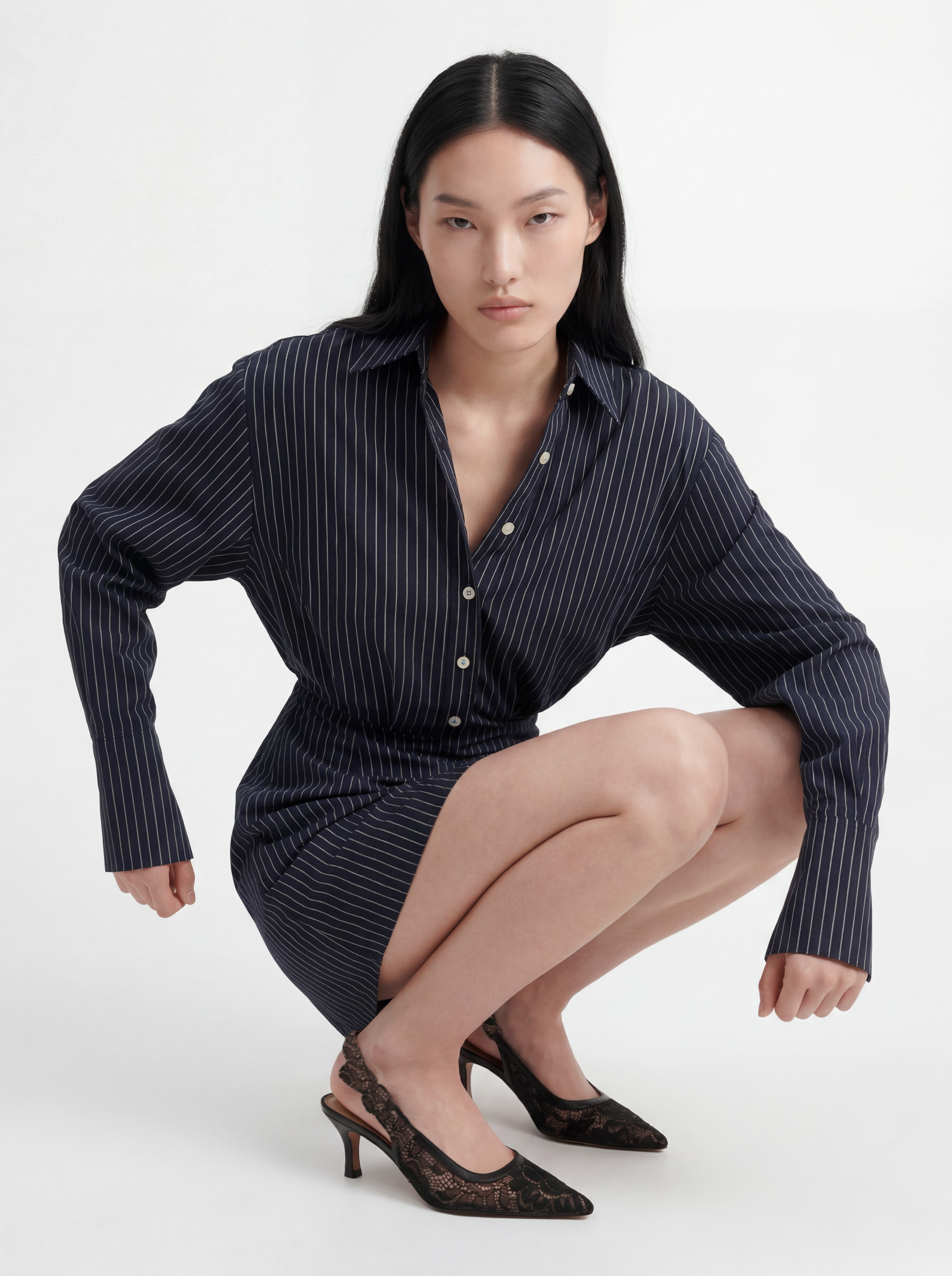 Model wearing L’ABITO CAMICIA SPALLE SCOLPITE by ORNELLA COLICCHIO in a seated pose with legs to the side, straight posture, sleeves hanging naturally and looking into the camera