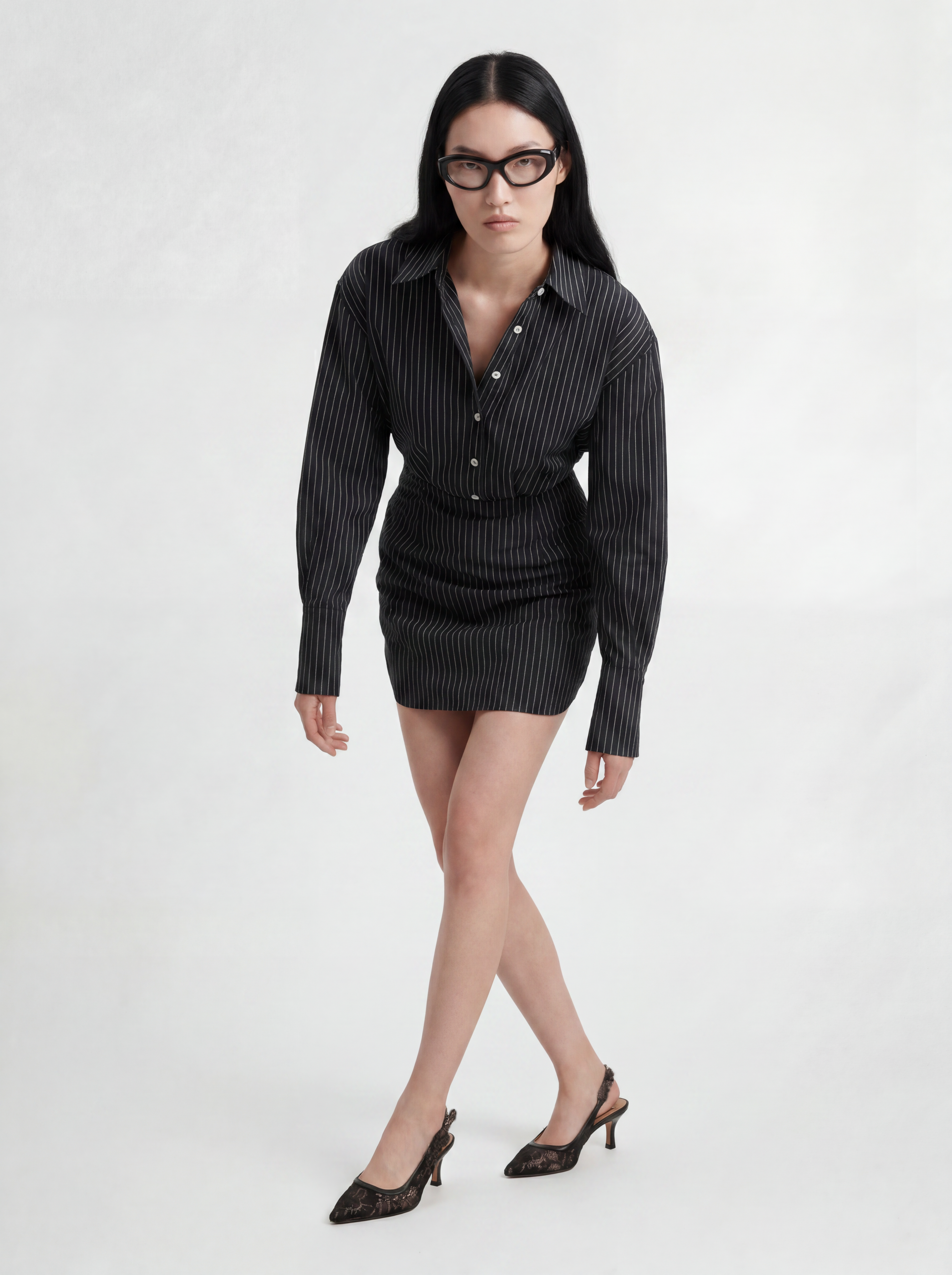 Front view of model wearing L’ABITO CAMICIA SPALLE SCOLPITE by ORNELLA COLICCHIO, leaning slightly forward with crossed legs, showing the tailored collar and body-close form