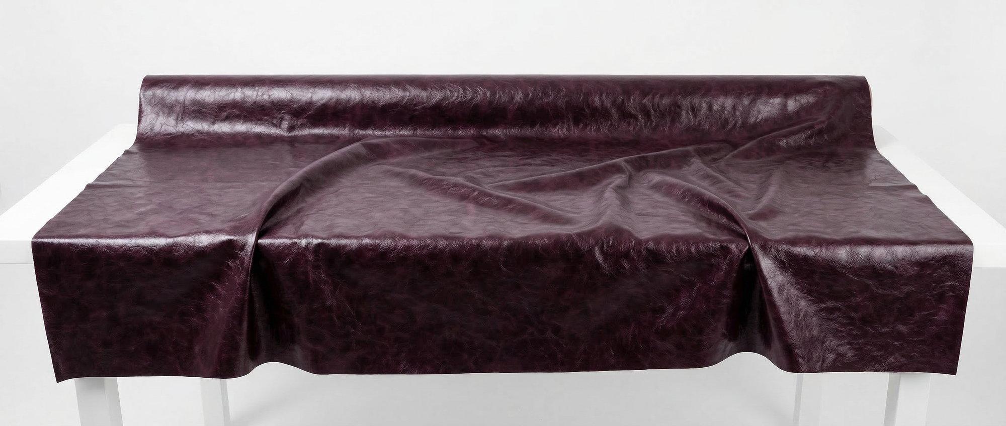 Large fabric roll for LA GIACCA CORTA BORDEAUX by ORNELLA COLICCHIO on a white studio table, unrolled toward the camera to reveal the bordeaux material texture