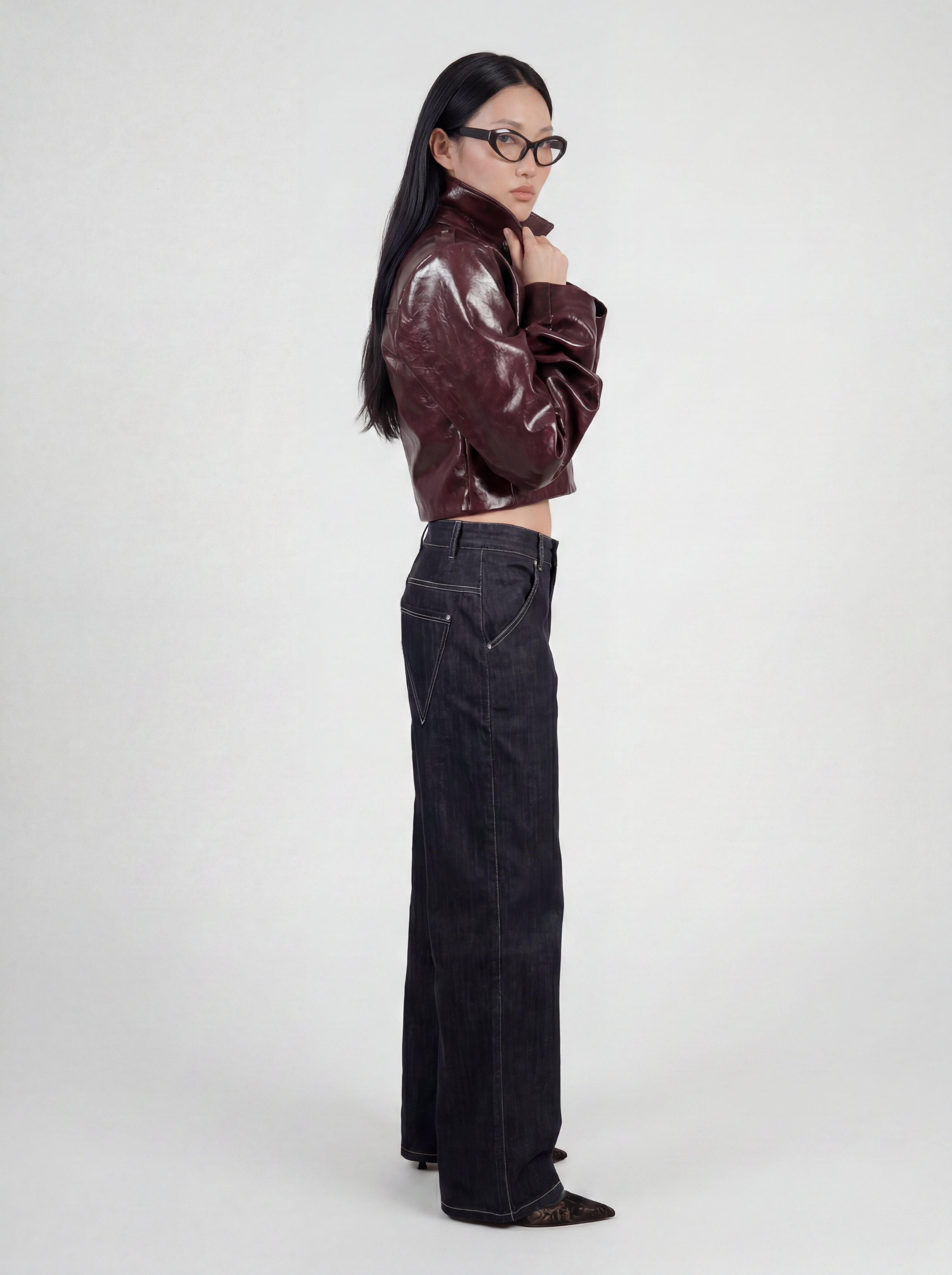 Side view of model wearing LA GIACCA CORTA BORDEAUX by ORNELLA COLICCHIO, holding the collar with both hands, looking into the camera and wearing IL DENIM TRIANGOLO