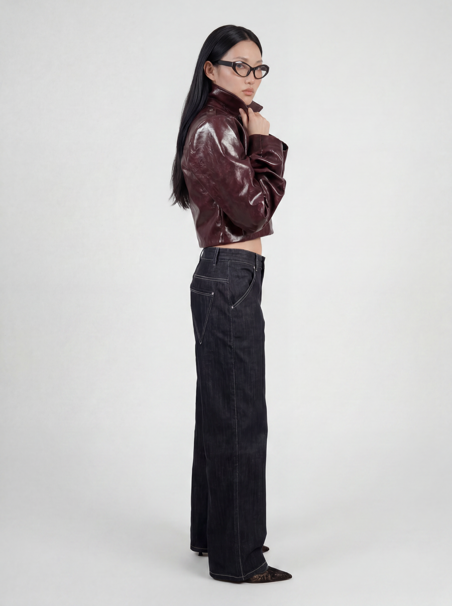 Side view of model wearing LA GIACCA CORTA BORDEAUX by ORNELLA COLICCHIO, holding the collar with both hands, looking into the camera and wearing IL DENIM TRIANGOLO