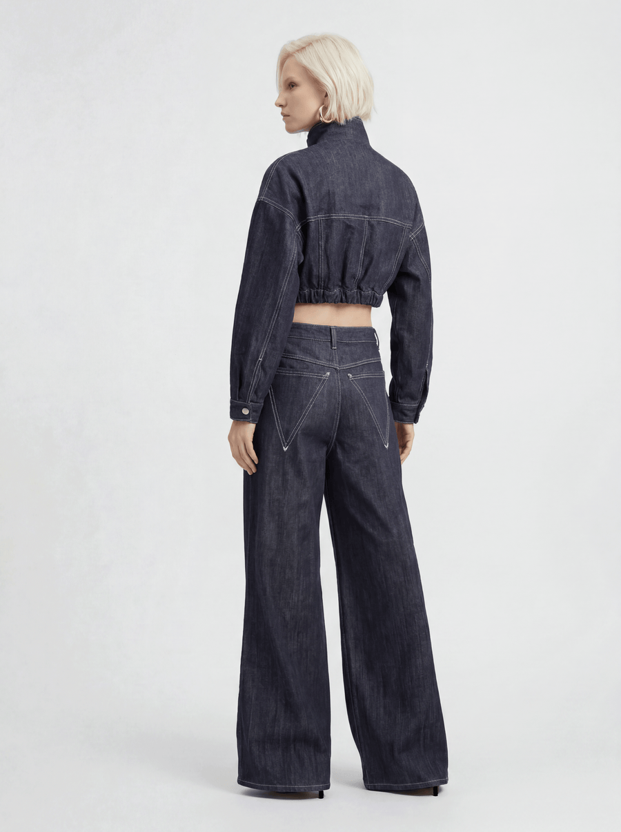 Back view of model wearing LA GIACCA CORTA IN DENIM and IL DENIM TRIANGOLO by ORNELLA COLICCHIO, looking to the side and showing the back of the denim jacket and triangular pockets