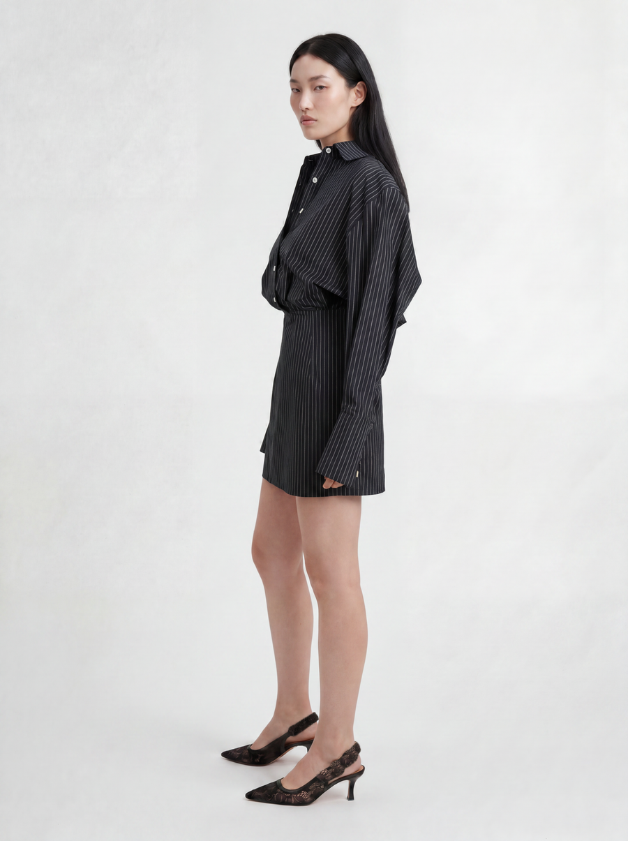 Side view of model wearing L’ABITO CAMICIA SPALLE SCOLPITE by ORNELLA COLICCHIO, looking into the camera and showing the wide shirt construction, backward fall, long cuff and body-close silhouette