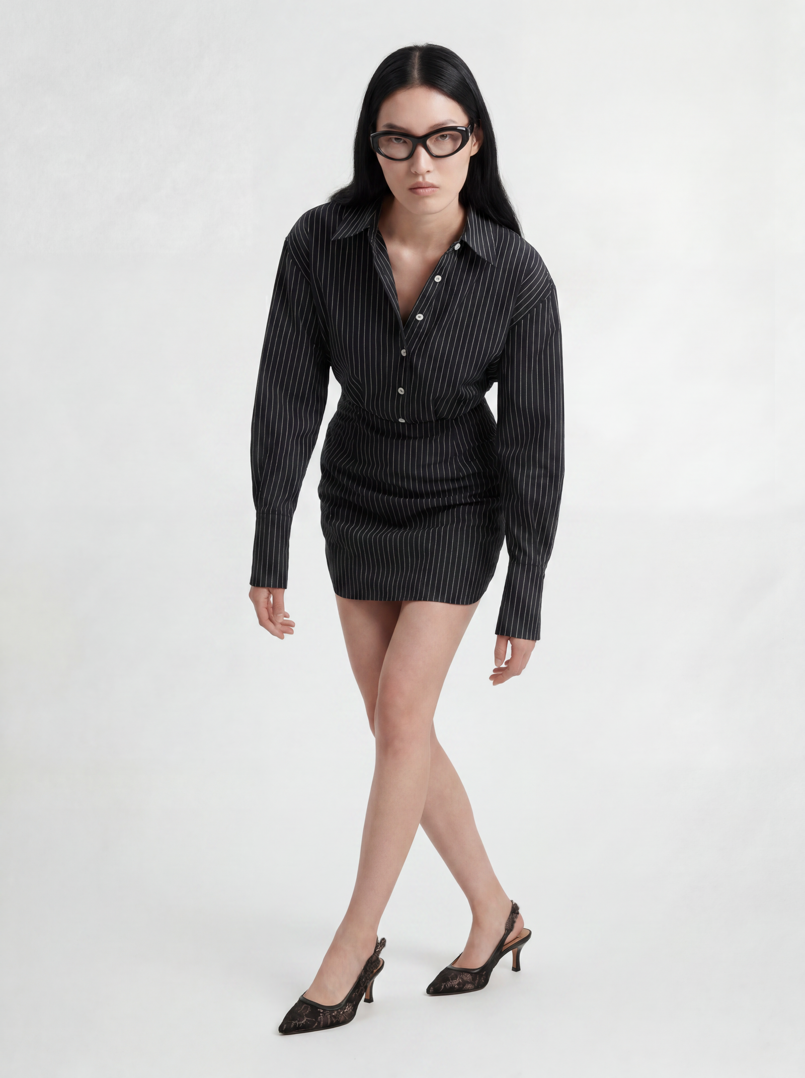Front view of model wearing L’ABITO CAMICIA SPALLE SCOLPITE by ORNELLA COLICCHIO, leaning slightly forward with crossed legs, showing the tailored collar and body-close form