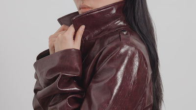 Campaign video of model wearing LA GIACCA CORTA BORDEAUX by ORNELLA COLICCHIO, holding the collar with sculptural sleeves visible and looking into the camera from a slow side pose